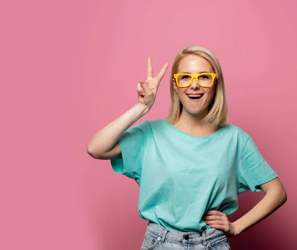 Krásná blondýna žena ve žlutých brýlích na růžovém pozadí — Stock fotografie