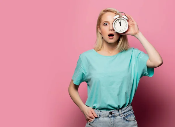 Belle femme blonde avec réveil sur fond rose — Photo