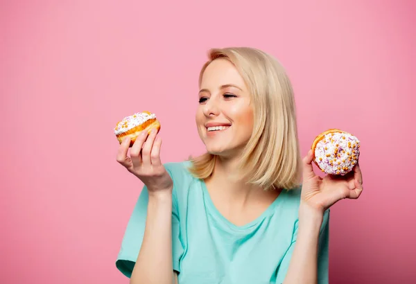 Mooie blonde vrouw met donut op roze achtergrond — Stockfoto