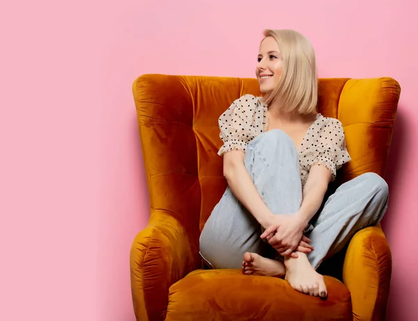 Stijl blonde vrouw zitten in een vintage fauteuil op roze backgro — Stockfoto