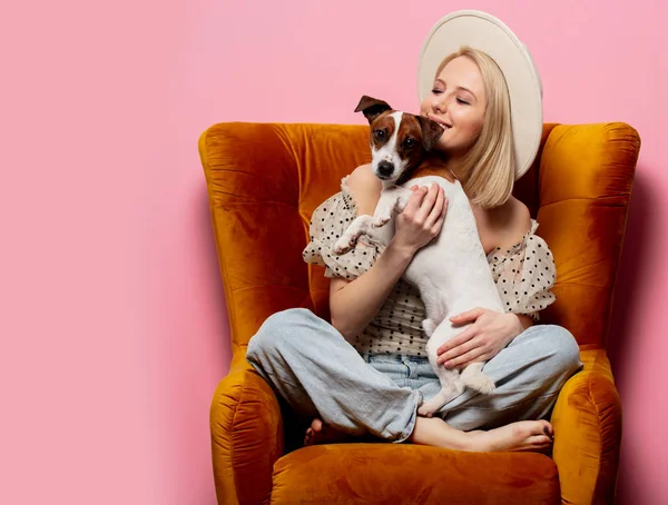 Hermosa mujer rubiacon un perro en un sillón sobre fondo rosa — Foto de Stock