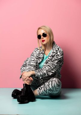 Beautiful woman in style clothes and sunglasses sitting on blue 