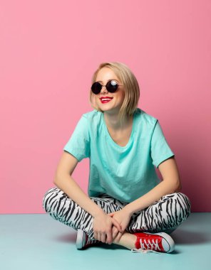 Beautiful woman in style clothes and sunglasses sitting on blue 