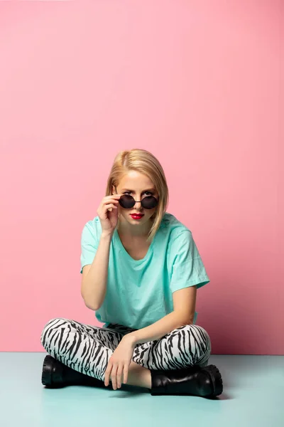 Mooie vrouw in stijl kleding en zonnebril zitten op blauw — Stockfoto