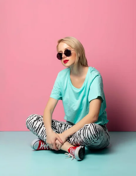 Mulher bonita em roupas de estilo e óculos de sol sentado em azul — Fotografia de Stock