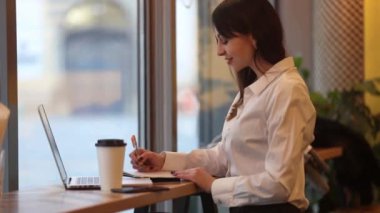 Laptop bilgisayarı olan esmer bir kadın kafede çalışıyor.