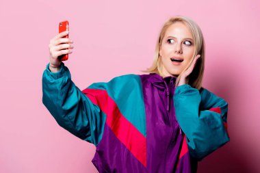 Güzel sarışın kadın pembe arka planda selfie çekiyor.