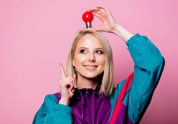 Donna bionda in abito sportivo anni '90 con lampadina su sfondo rosa — Foto Stock