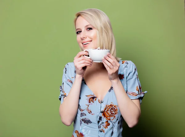 Блондинка в одязі з чашкою кави на зеленому фоні. вул — стокове фото