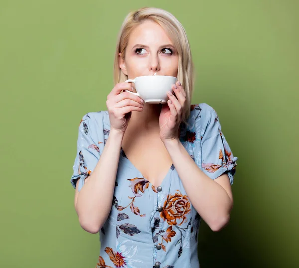 Blonde woman in dress with cup of coffee on green background. St — Stock Photo, Image