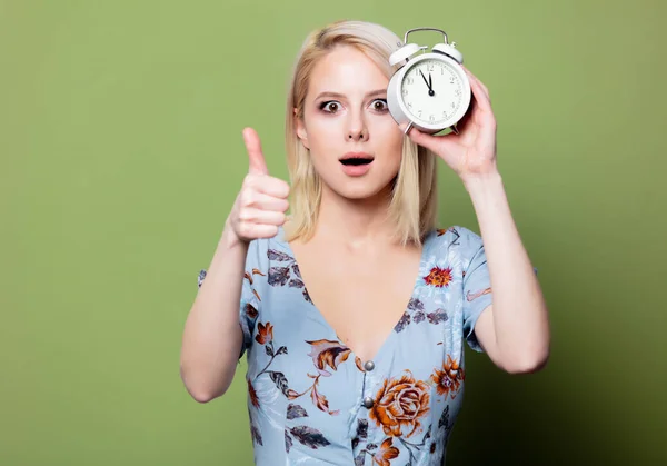 Blonde woman with alarm clock on green background — Stock Photo, Image