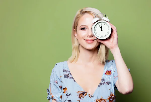 Blonde woman with alarm clock on green background — Stock Photo, Image