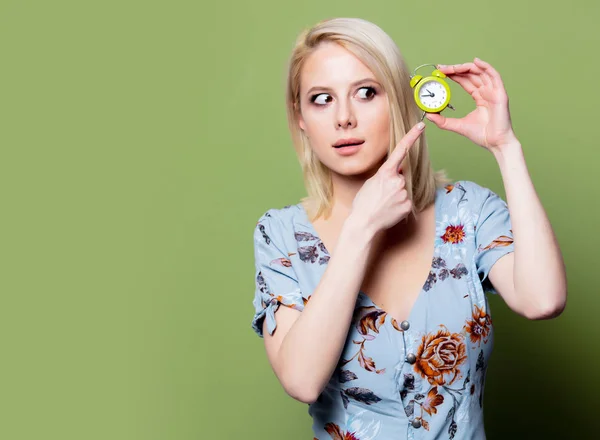 Mulher loira com despertador no fundo verde — Fotografia de Stock