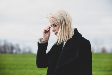 Siyah ceketli, kırsalda gözlüklü bir kadın. 