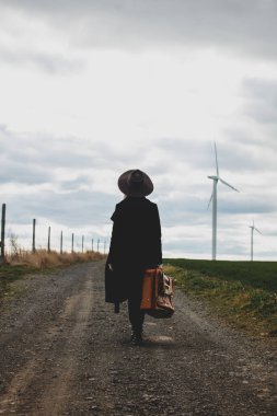 Kırsalda şapkalı ve valizli bir kadın. 