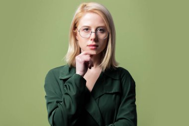 Pelerinli zarif sarışın kadın ve yeşil arka planda yuvarlak gözlükler. 