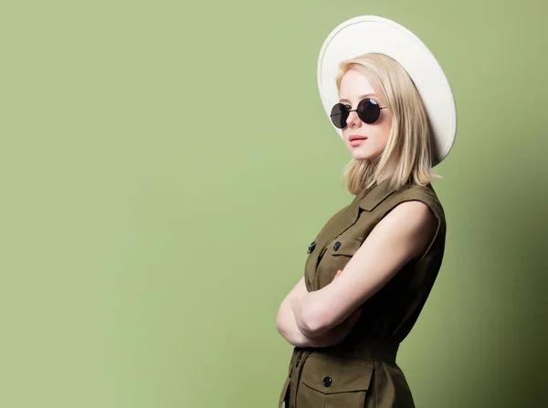 スタイルブロンド女性でサングラス 帽子とサンドレス上の緑の背景 — ストック写真