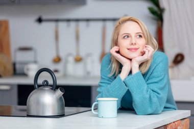 Mutfakta bir fincan kahveyle sarışın kadın. 