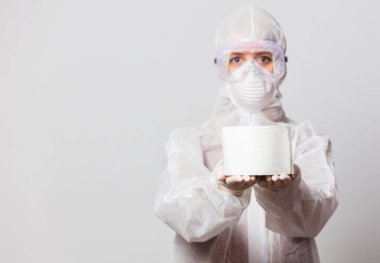 Koruyucu takım elbiseli genç bir doktor ve beyaz arka planda tuvalet kağıdı olan maskeli gözlükler.