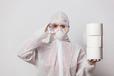 Koruyucu takım elbiseli genç bir doktor ve beyaz arka planda tuvalet kağıdı olan maskeli gözlükler.