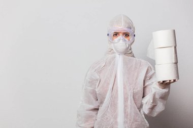 Koruyucu takım elbiseli genç bir doktor ve beyaz arka planda tuvalet kağıdı olan maskeli gözlükler.