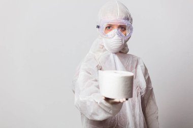 Koruyucu takım elbiseli genç bir doktor ve beyaz arka planda tuvalet kağıdı olan maskeli gözlükler.