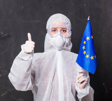 Korunma giysisi içindeki kadın doktor ve maske takan gözlüklü kadın AB bayrağı taşıyor