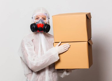 Koruyucu giysili kadın postacı ve maskeli gözlüklü kadın teslimat kutuları tutuyor.