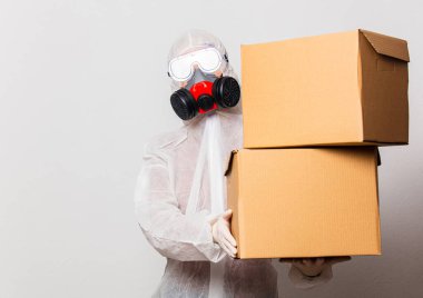 Koruyucu giysili kadın postacı ve maskeli gözlüklü kadın teslimat kutuları tutuyor.