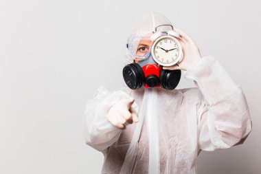 Koruyucu giysili kadın doktor ve maskeli gözlüklü kadın alarmlı saat tutuyor. 