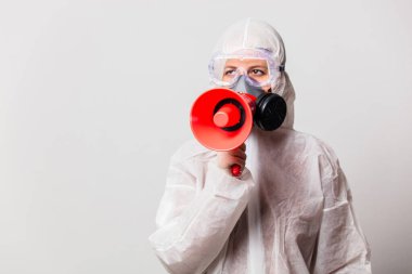Korunma giysisi ve maskeli gözlüklü kadın doktor megafon tutuyor. 