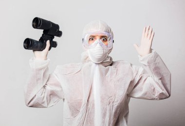 Koruyucu giysili ve gözlüklü genç bir doktor, beyaz arka planda dürbünlü bir maske.