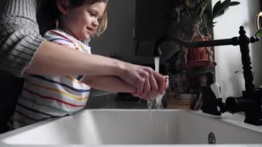 Anne, toddelr çocuğuyla ellerini yıkıyor.