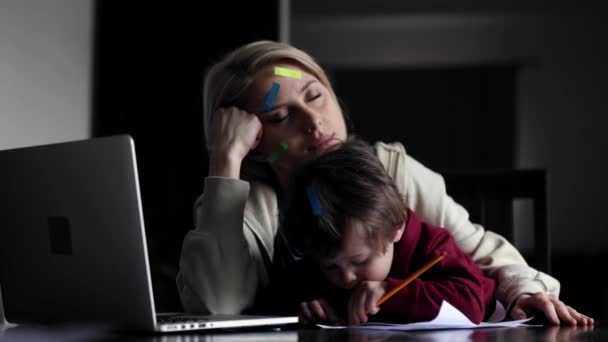 幼い母親は子供と一緒に自宅のコンピュータで働いています — ストック動画
