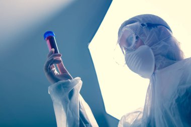 Koruma giysilerindeki doktor COVID-19 aşısını tutuyor.