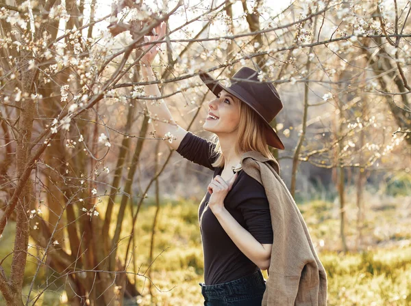 日落时戴着帽子在樱花园里的时髦姑娘 — 图库照片