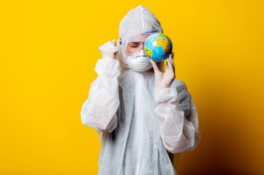 Koruyucu giysi ve maske giyen sağlık ekibi Dünya 'yı sarı arka planda tutun.