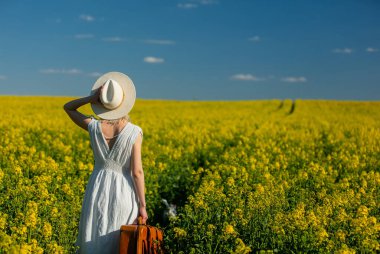 Bahar zamanı kolza tohumu tarlasında bavullu güzel bir kadın. 