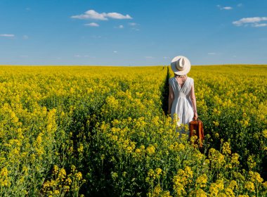 Bahar zamanı kolza tohumu tarlasında bavullu güzel bir kadın.