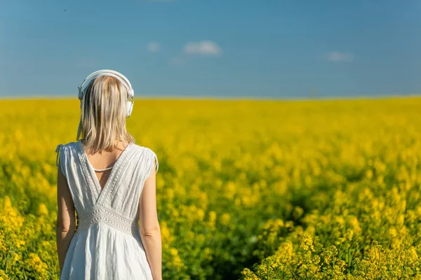 春天的时候 美丽的女人带着耳机站在菜田里 — 图库照片