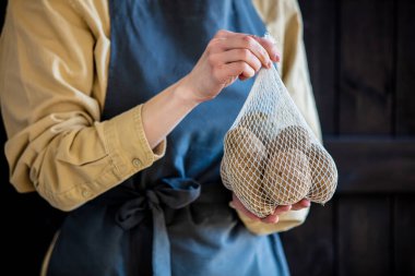 Önlüklü kadın sepetinde patates tutuyor. 