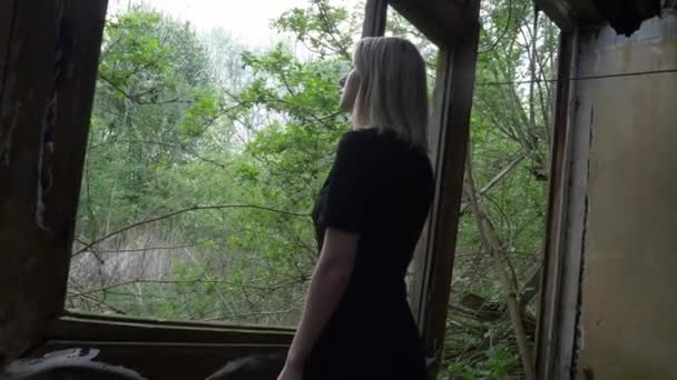 女性は庭の窓の近くのカメラに背を向けて立つ — ストック動画