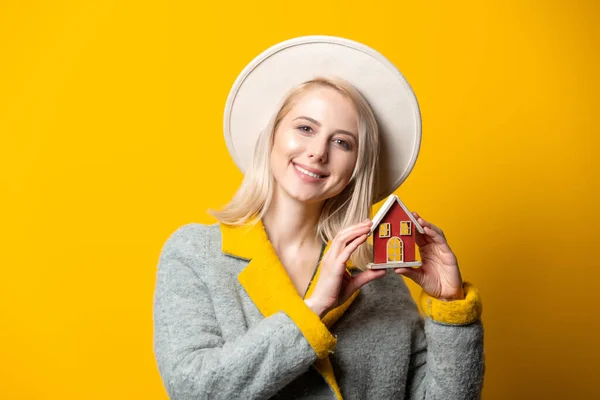 Estilo Mulher Loira Chapéu Casaco Com Casa Brinquedo Fundo Amarelo — Fotografia de Stock