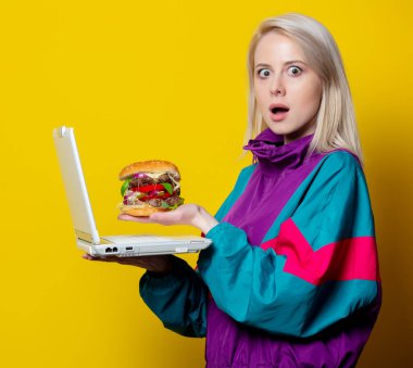 80 'lerin kıyafetleri içinde hamburger ve defter siparişi veren bir kız.