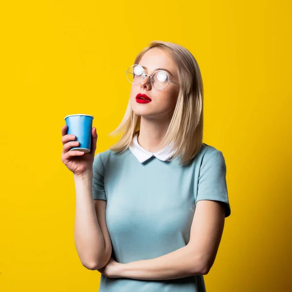 Menina Loira Vestido Azul Óculos Copo Papel Fundo Amarelo — Fotografia de Stock