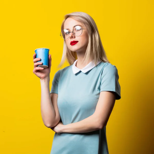 Sarı Arka Planda Mavi Elbiseli Gözlüklü Kağıt Bardaklı Sarışın Kız — Stok fotoğraf