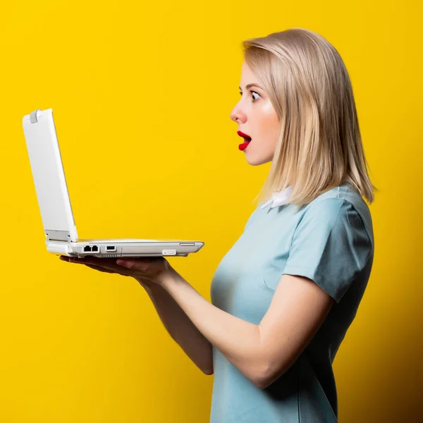 ブロンド女の子で青ドレスでラップトップコンピュータ上の黄色の背景 — ストック写真
