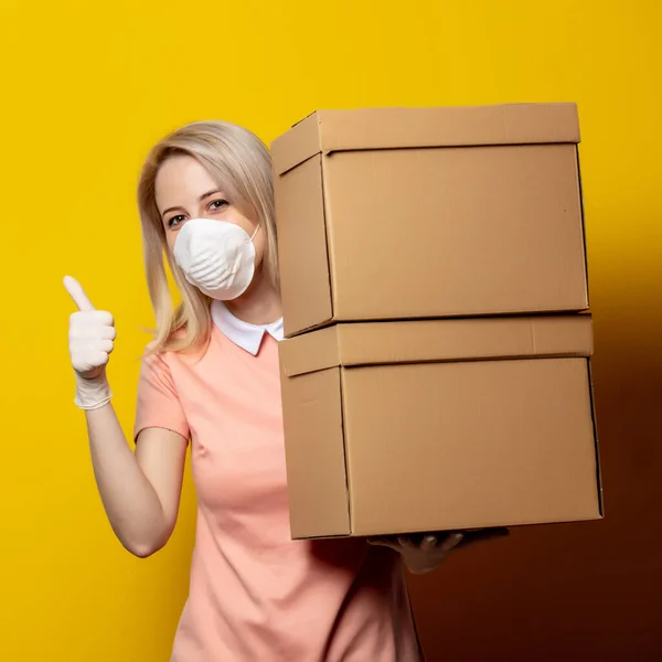 Sarı Arka Planda Teslimat Kutuları Olan Maskeli Sarışın Kız — Stok fotoğraf