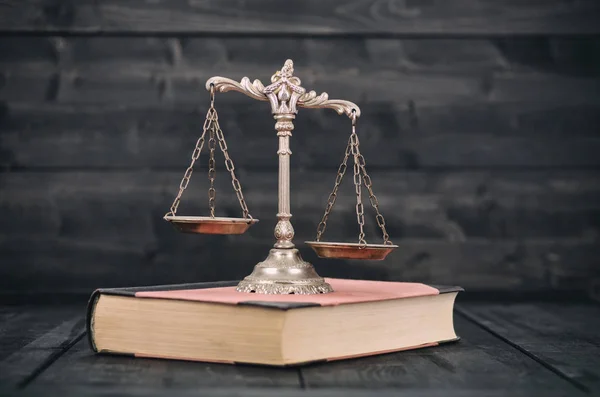 Scales of Justice and law books on a wooden background.