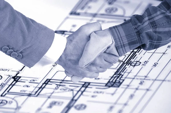 Worker and businessman shaking hands over house renovation plans — Stock Photo, Image